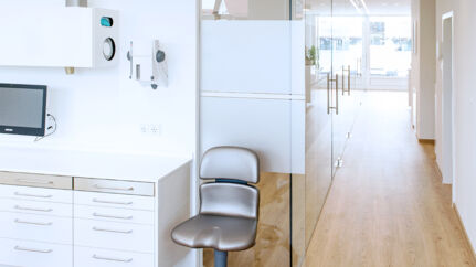 Hallway in a dentist's office, wooden floor and white furniture; in the foreground a swivel chair.