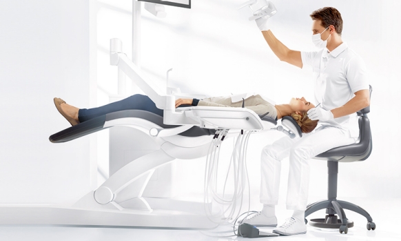 Dentist sitting on dental stool while treating patient