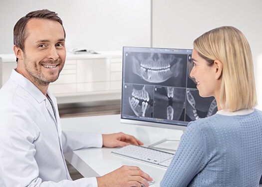 Dentist at a monitor with patient and x-ray pictures