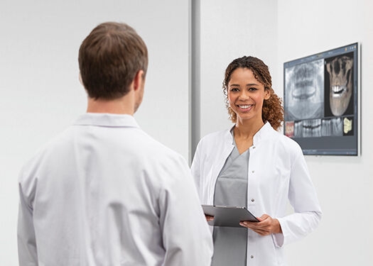 Dentist smiling into the camera while talking to a collegue at a monitor