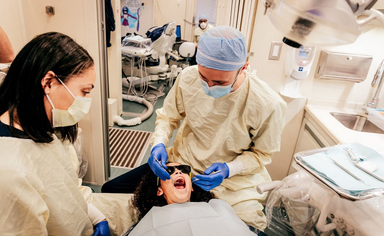 A girl receiving dental treatment from a dentists and assistant.